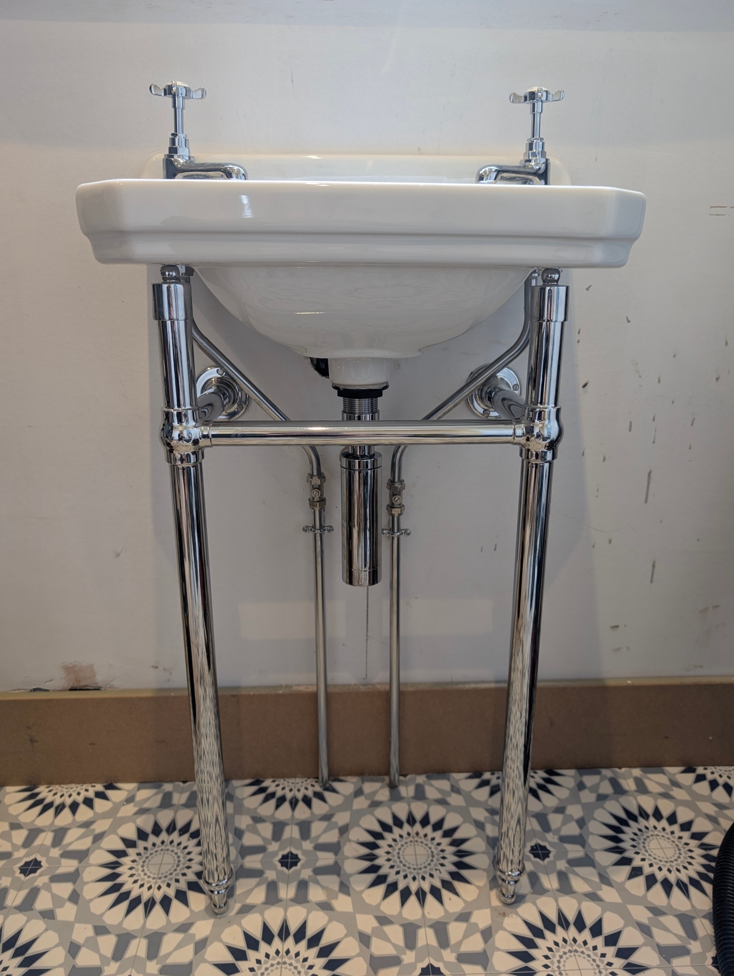 Traditional basin on chrome washstand over patterned floor tiles